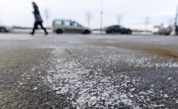 Close up or road salt on a sidewalk, cars and person walking in background.