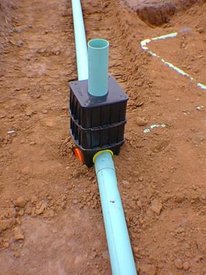 Blue pipes connecting to a black plastic box. System is partially buried in reddish-brown soil.