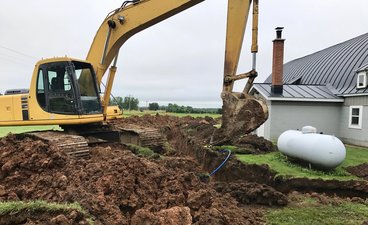 Excavator digging trenches along a rural property 