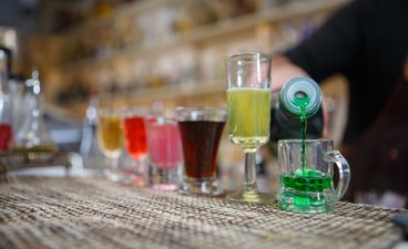 Glasses of colorful alcohol being poured at a bar